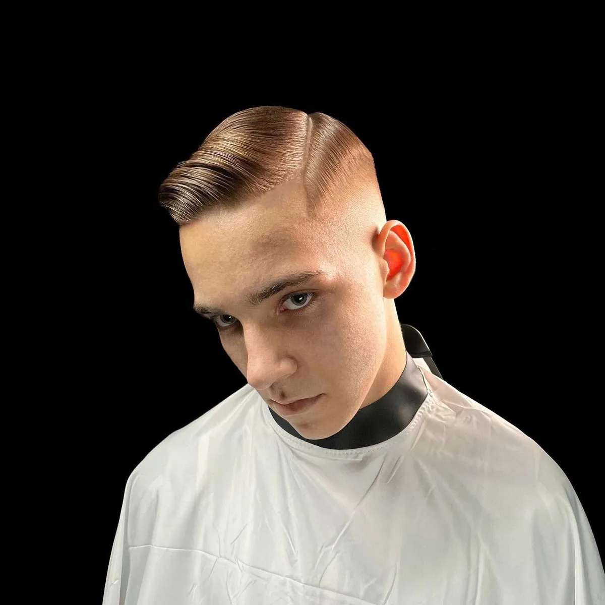 Jauns vīrietis ar side part griezumu un mid fade pāreju skatās kamerā