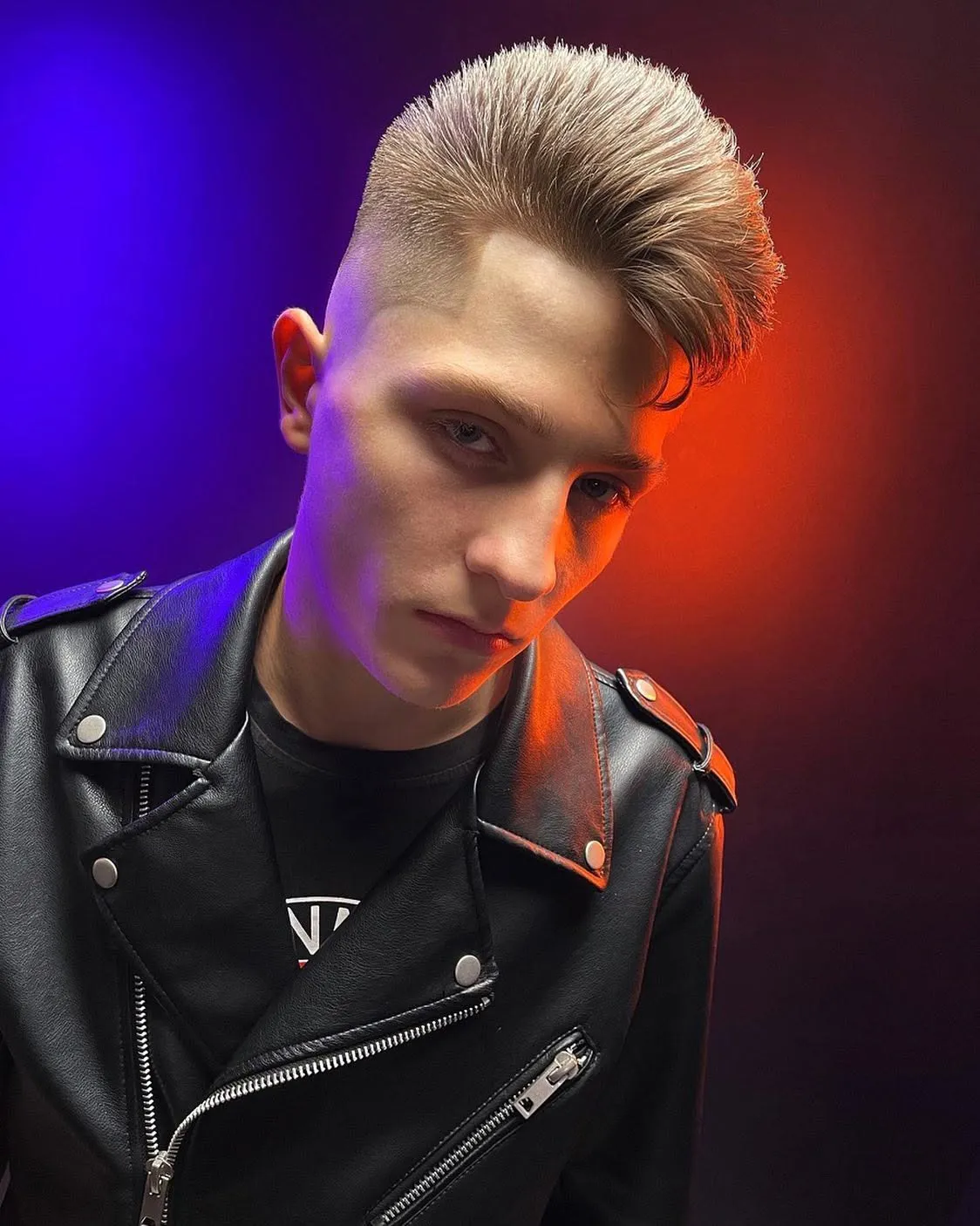 Moderns rockabilly griezums ar augstu, ieveidotu matu augšdaļu, vīrietis ādas jakā sarkanzilā gaismā